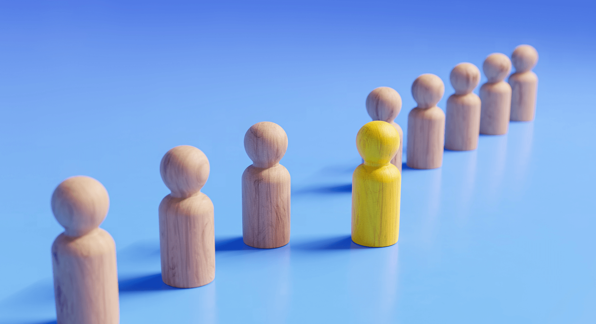 Figuras de madera forman una línea diagonal sobre un fondo azul, con una figura amarilla un paso adelante.
