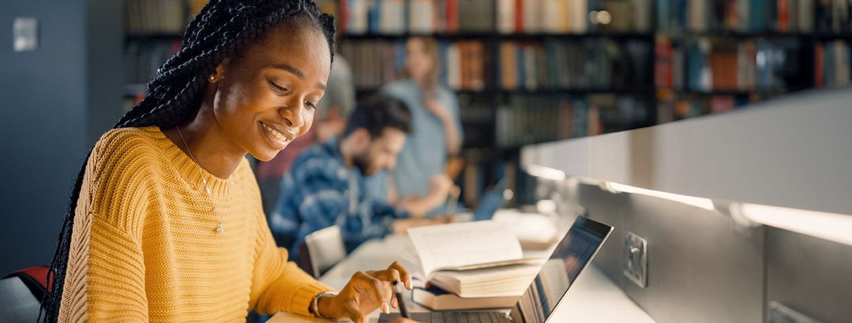 Biblioteca Universitaria: Chica negra talentosa usa laptop y toma notas