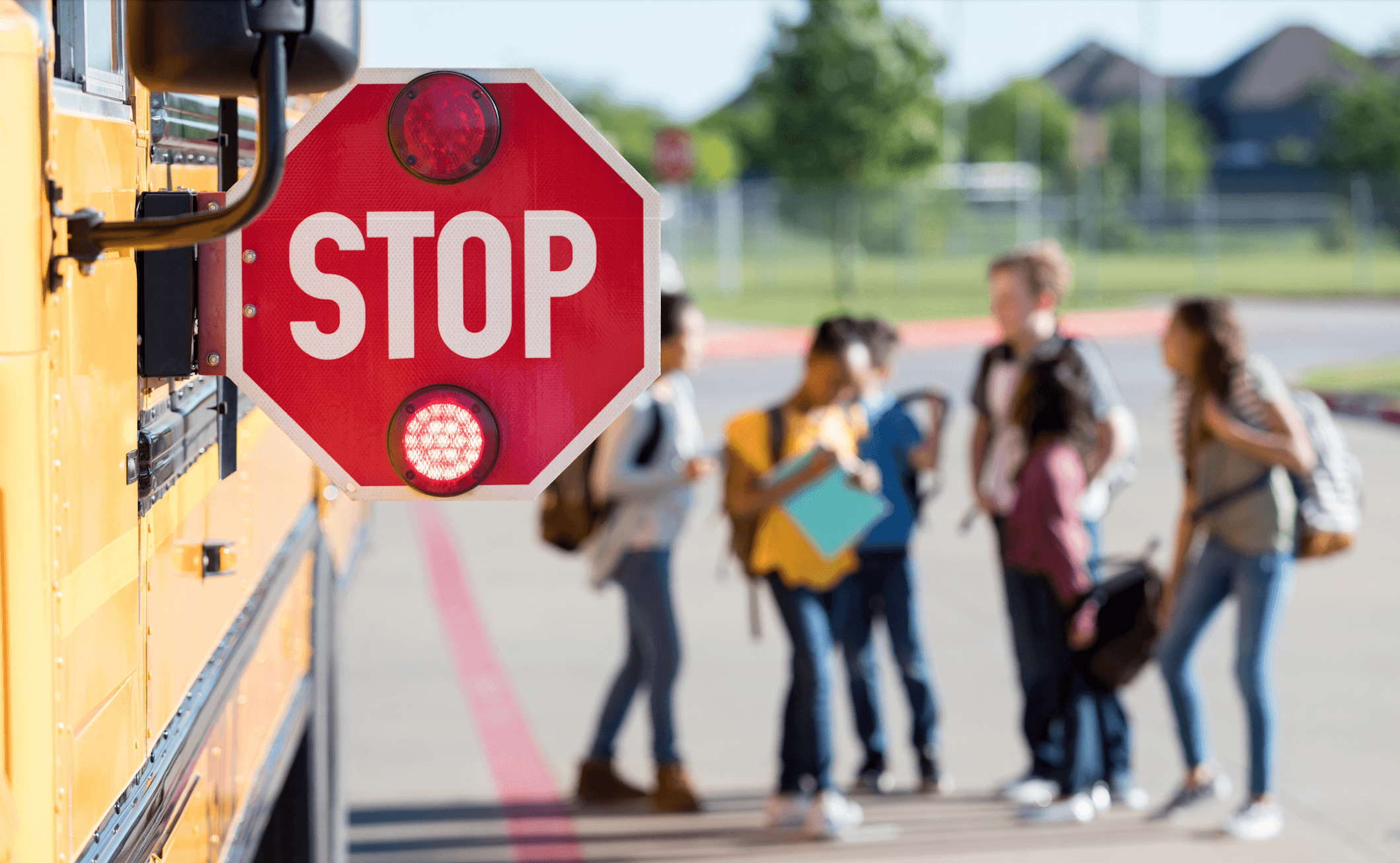 Imagen destacada del blog. Foto de una señal de STOP sobresaliendo del lateral de un autobús escolar, con estudiantes de secundaria conversando borrosos al fondo.