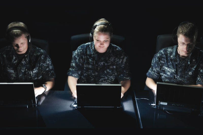 Tres miembros de la Armada, vestidos de uniforme, trabajando frente a los ordenadores