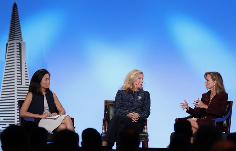 Tres mujeres en una mesa redonda sobre un escenario con el perfil urbano de la ciudad como telón de fondo