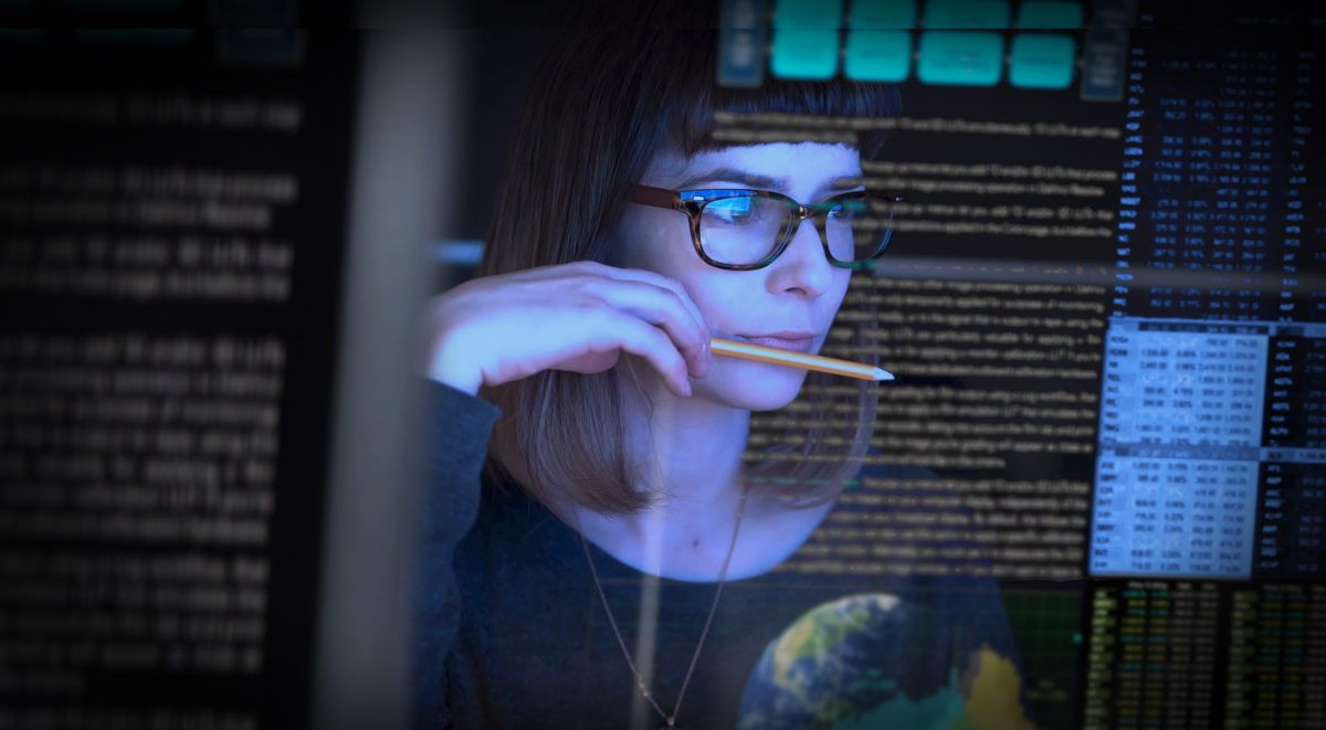 Mujer profesional con chaqueta azul que sostiene cables de datos, con la sala de servidores como fondo