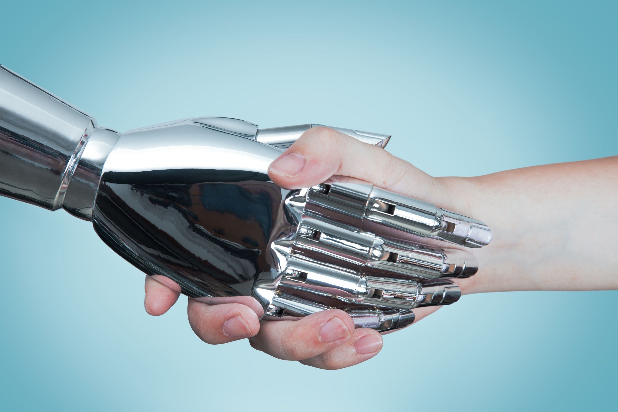 Una fotografía en primer plano de un apretón de manos entre un robot de inteligencia artificial y un ser humano.