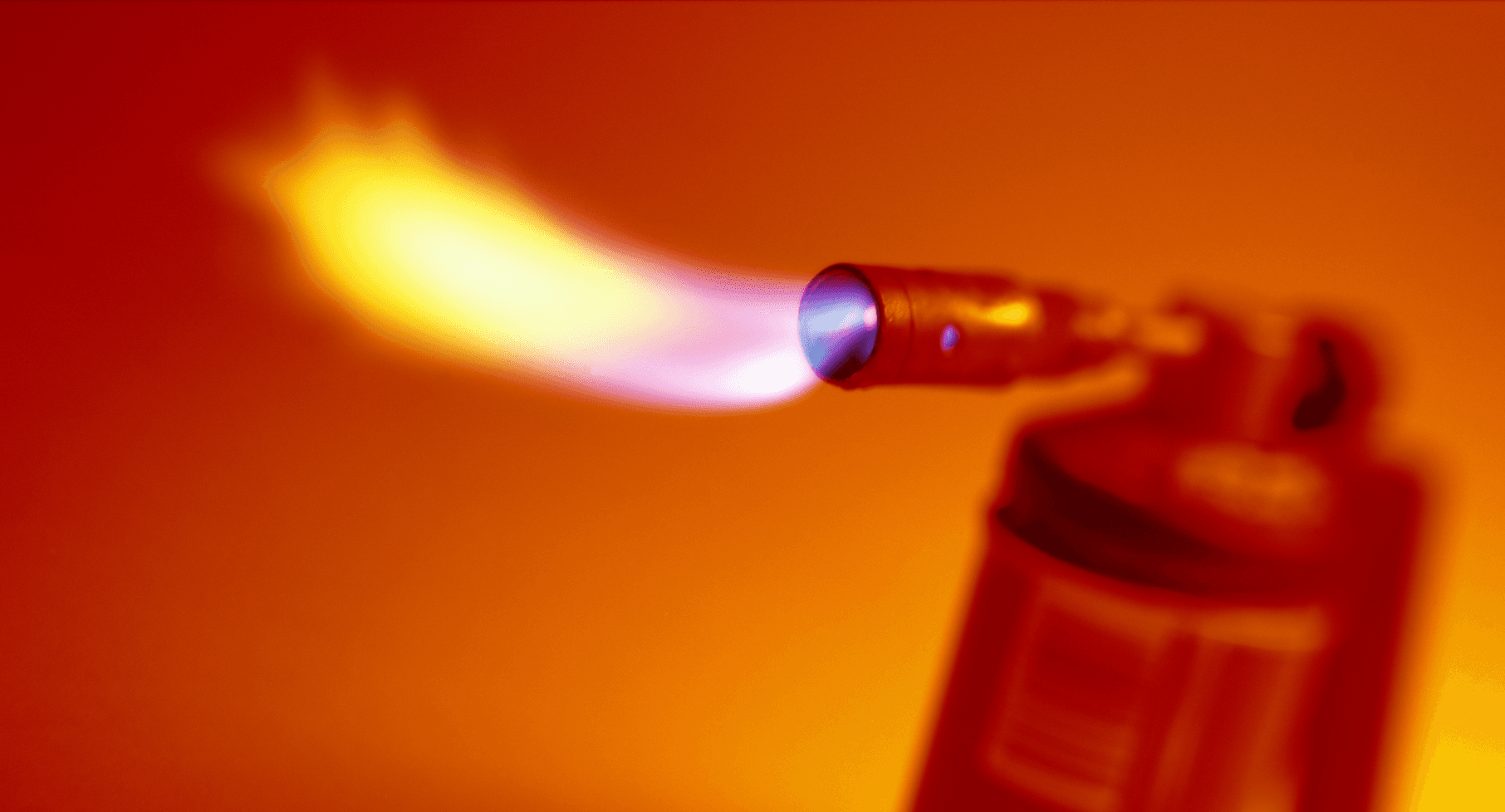 A photo of a red blowtorch spewing flames, and set against an orange backdrop.