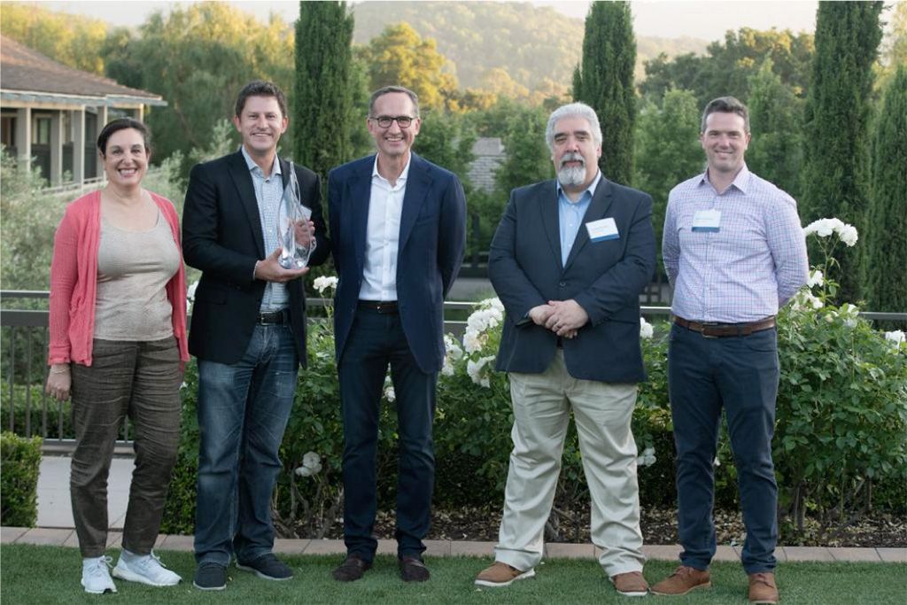 Fotografía de cinco personas en una entrega de premios con un pintoresco paisaje al aire libre como telón de fondo