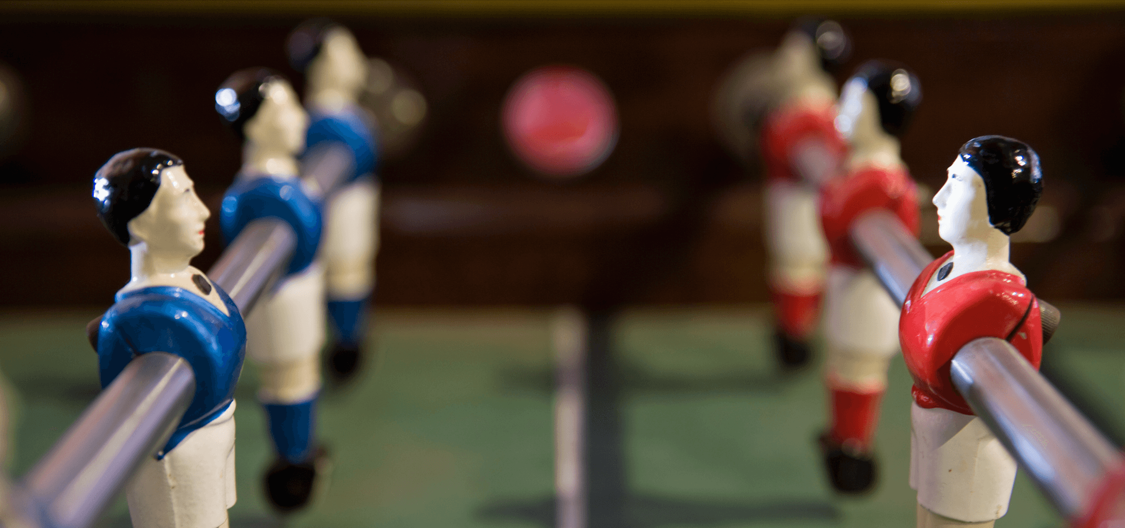 Closeup image of a foosball table, with plastic figures on metal rods facing off in blue and red jerseys.