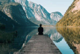 Persona sentada en un embarcadero con vistas a un lago de montaña y a un paisaje boscoso