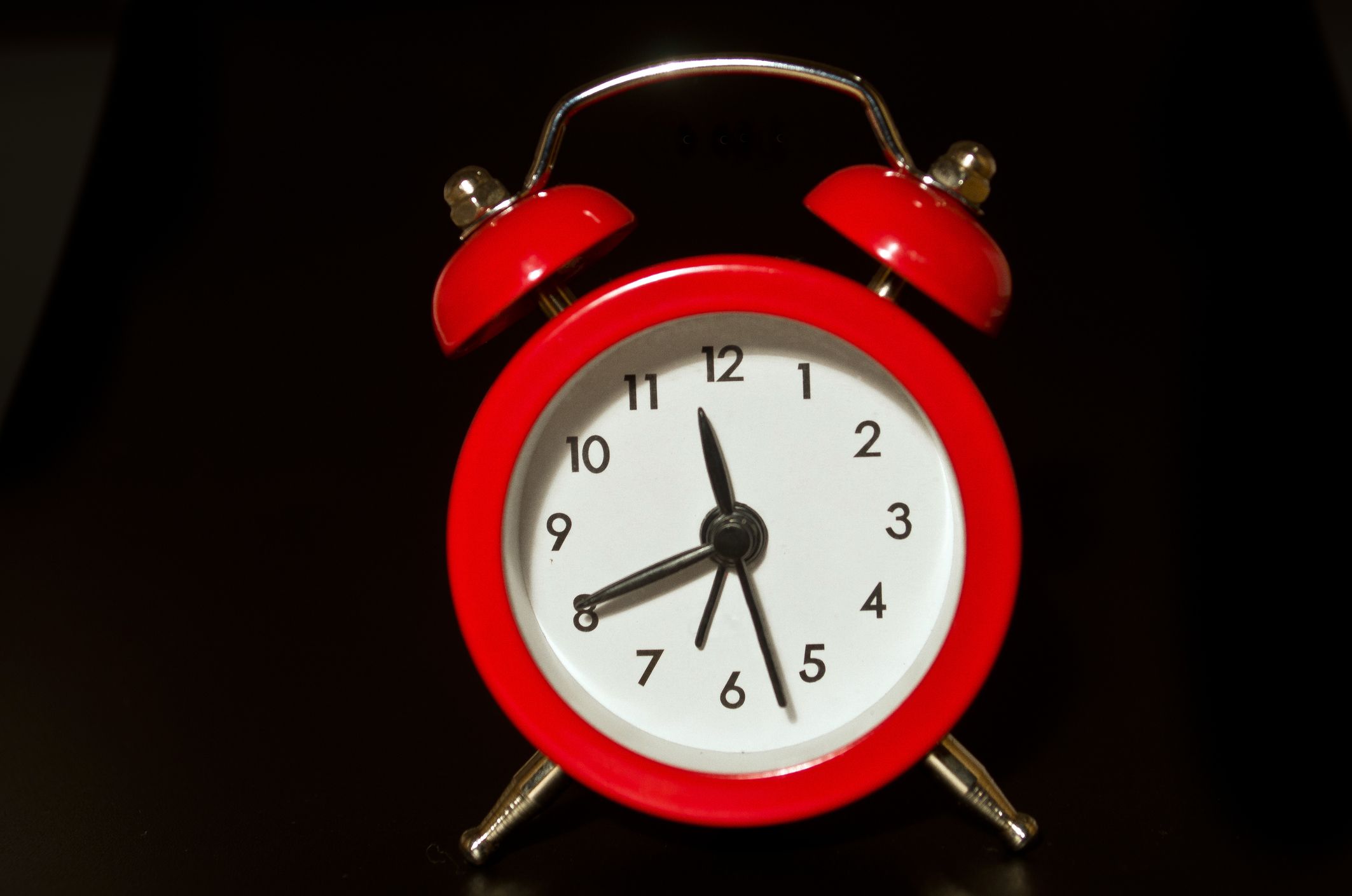 Un brillante reloj despertador rojo se alza sobre un fondo negro—las manecillas del reloj muestran que la hora es 11:41.
