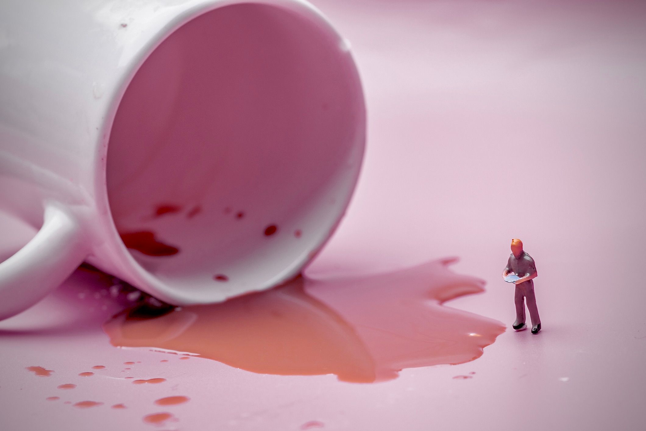 Una imagen de una figura humana en miniatura evaluando café derramado de una taza volcada.