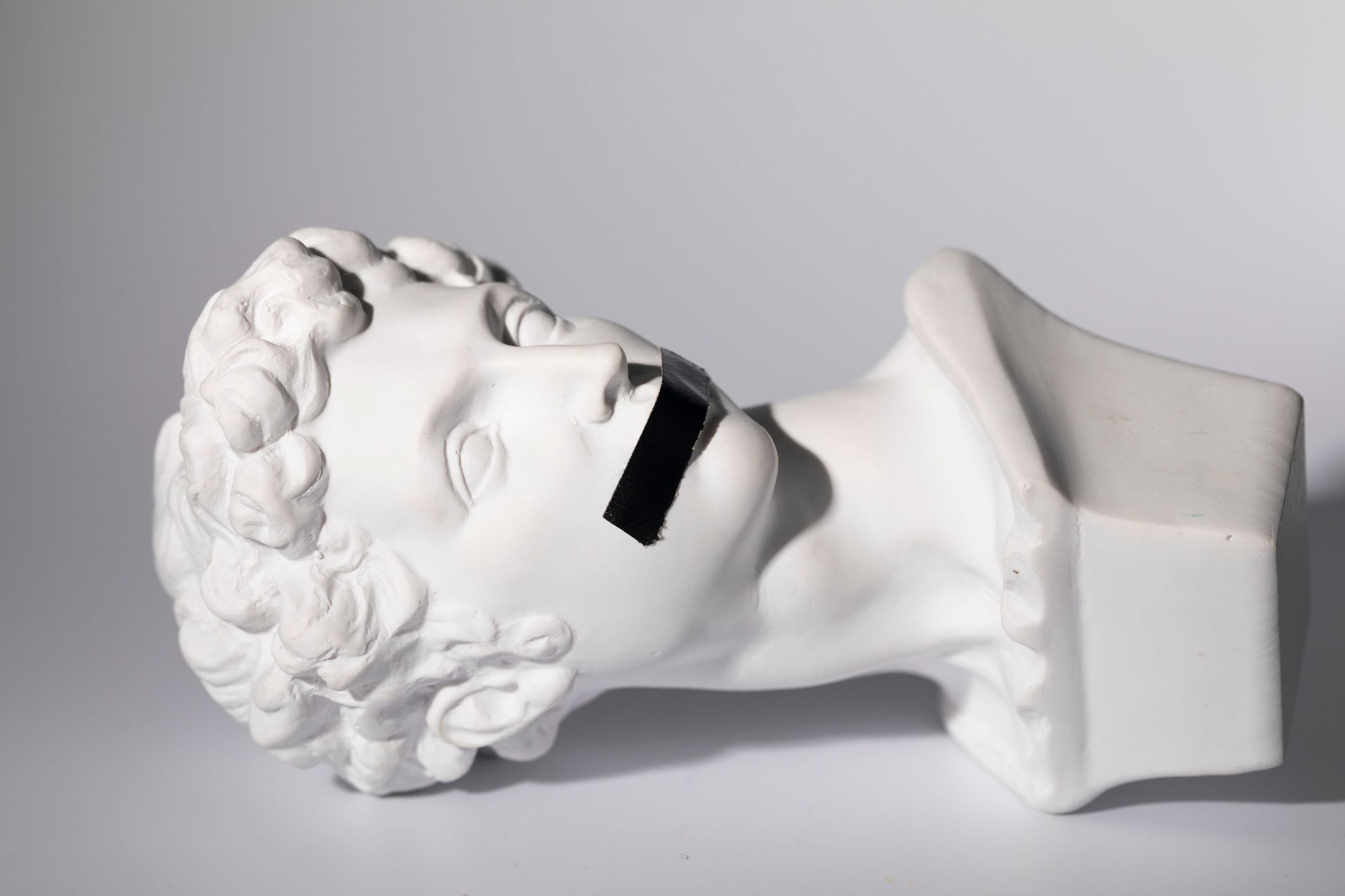 Foto de una escultura medieval de piedra blanca de la cabeza de un joven, con cinta negra cubriendo la boca.